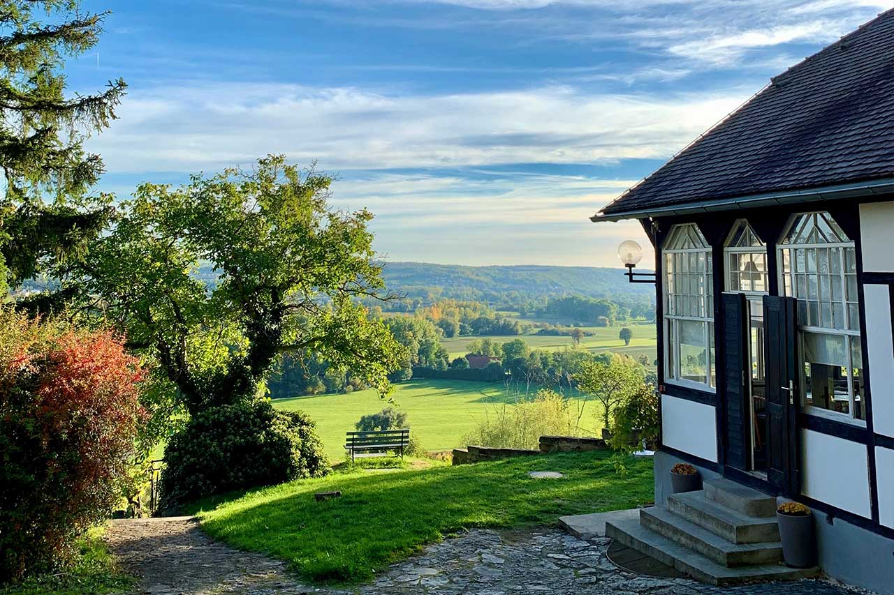 Blick von der Akademie Sonneck über grüne Hügel und Felder, mit Fachwerkhaus im Vordergrund – einst Rückzugsort für Künstler der DDR.